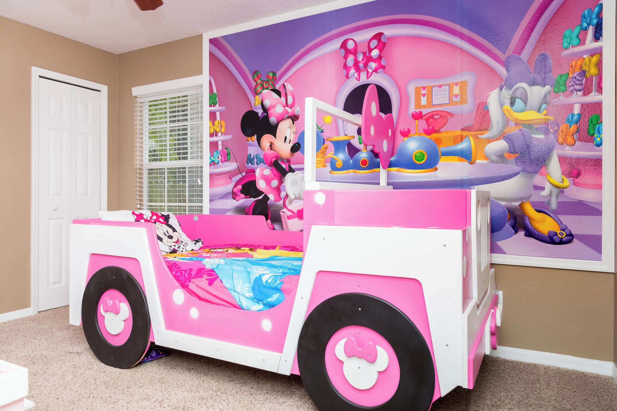 A pink and white playroom with Minnie Mouse and Daisy Duck decorations, a window with blinds, and a white door.