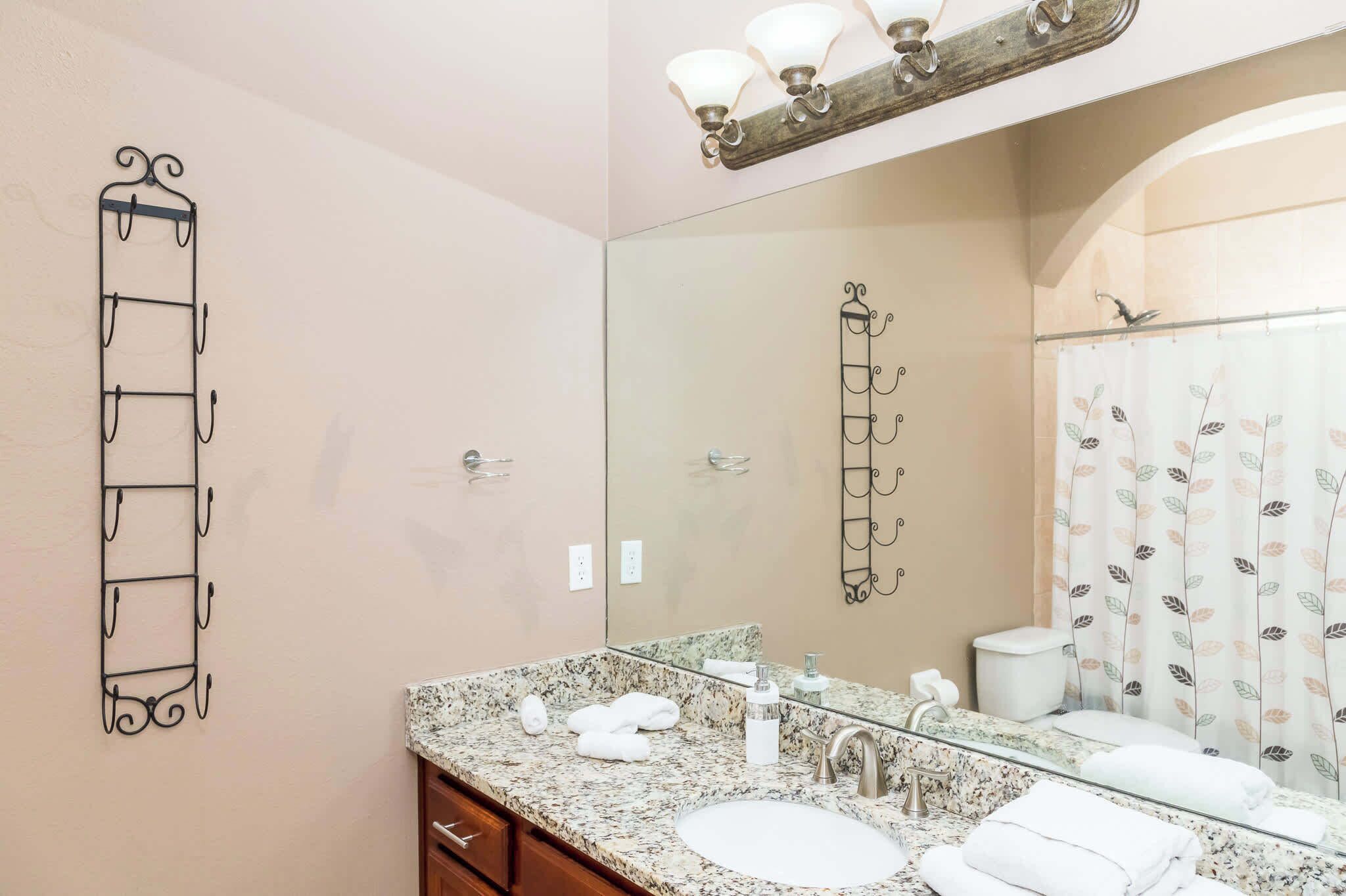 A bathroom with a granite countertop, two sinks, a mirror, a towel rack, and a shower curtain with a leaf pattern.