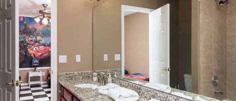 A bathroom with a large mirror, a sink, and a shower. There is a small step stool near the sink.