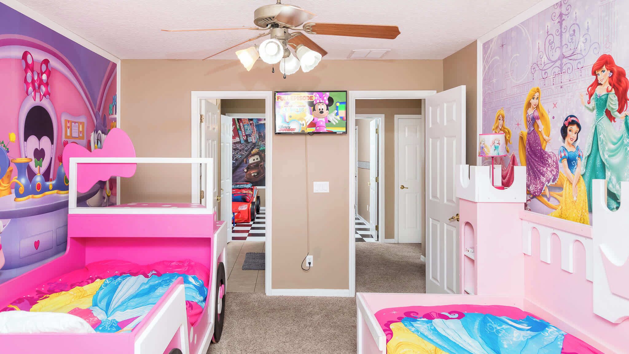 A children's room with bunk beds, a ceiling fan, and a TV on the wall.