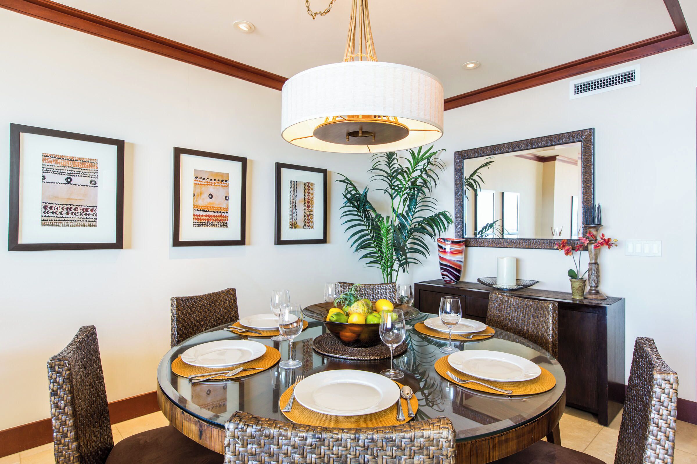 A dining area with a round glass table, wicker chairs, and a central fruit bowl.