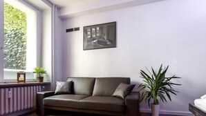 A modern living room with a dark brown leather sofa, a large potted plant, and a framed picture on the wall. - Apartment top location in Tiergarten, directly on the Spree, near Bellevue S-Bahn. (Berlin)