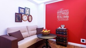 A living room with a sofa, a round table with a basket of fruit, and a red wall with a welcome sign. - Apartment top location in Tiergarten, directly on the Spree, near Bellevue S-Bahn. (Berlin)