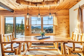 A wooden dining area with a large table, chairs, and a view of the outdoors. - Epic Views, Hot Tub, GameRoom & Bar, FirePit, Pets Ok, Sunday River (Bethel)
