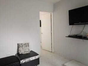 A room with a white door, a black TV on a shelf, and a black and white patterned box on a small table. - Cozy, comfortable and central apartment (Pereira)