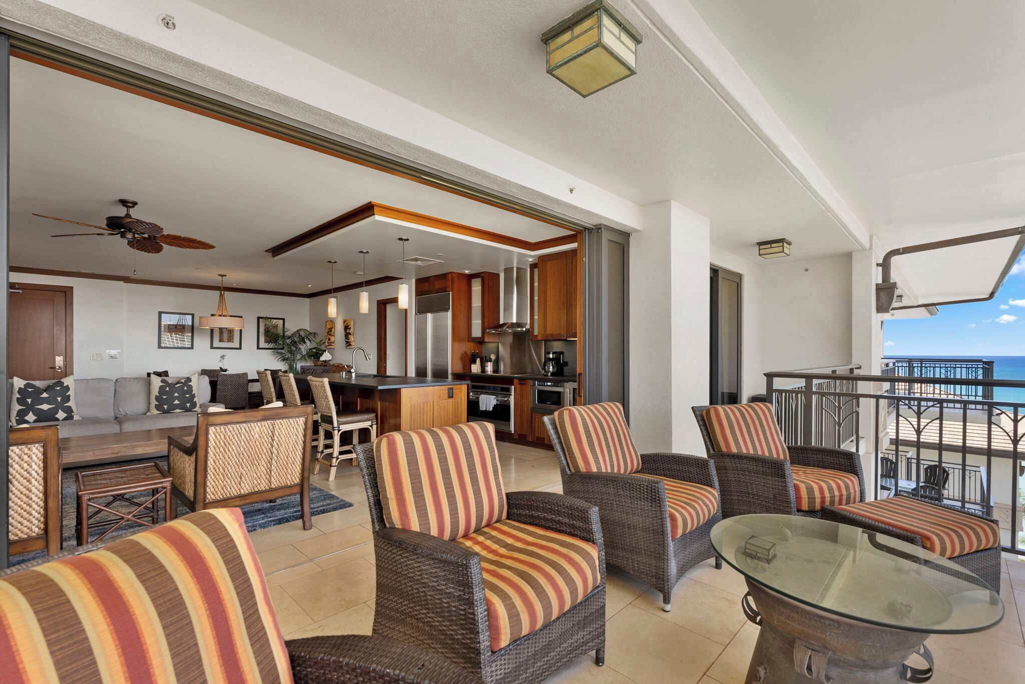 A spacious living area with wicker furniture, a glass coffee table, and a view of the ocean.