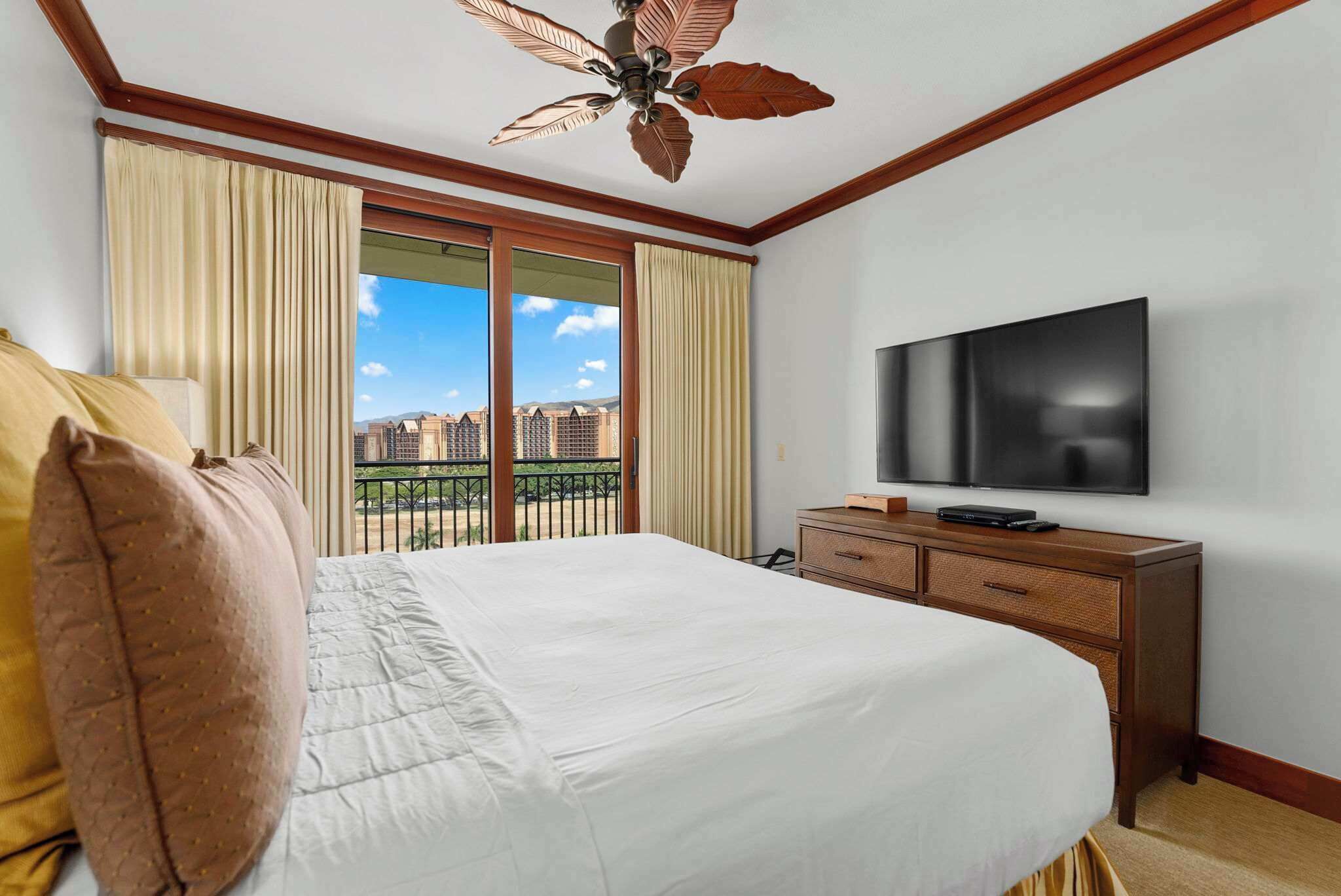 Une chambre d’hôtel dotée d’un grand lit, d’une télévision à écran plat, d’une commode en bois et d’un balcon offrant une vue sur la ville.
