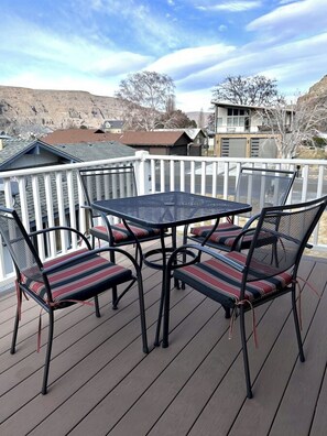 A deck with a table and chairs, a white railing, and a view of houses in the background.