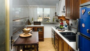 A compact kitchen with a dining area, a view of the city through the window, and a blue refrigerator. - Romantic attic with breathtaking views in the old town centre. (Napoli)
