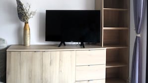 Una habitación con un mueble bajo de madera para el televisor, un televisor de pantalla plana, un gallo decorativo y un florero con plantas secas.