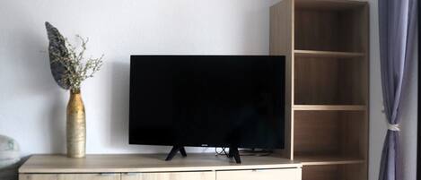Une pièce comprenant un meuble TV en bois, un téléviseur à écran plat, un coq décoratif et un vase contenant des plantes séchées.