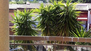 Un balcón con una silla a rayas, barandilla de cristal y vistas a una colina con edificios.