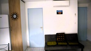 Una habitación con un armario de madera, una puerta blanca, un sofá gris con cojines y un aire acondicionado instalado en la pared.