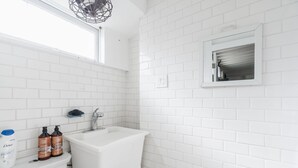 Une salle de bain avec des carreaux de céramique blancs rectangulaires, un lavabo blanc et deux bouteilles de shampoing Dove.