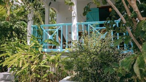 A covered outdoor seating area with a blue railing, surrounded by lush greenery. - Lagon - Charming Creole studio 2 steps from the sea (Sainte-Anne)