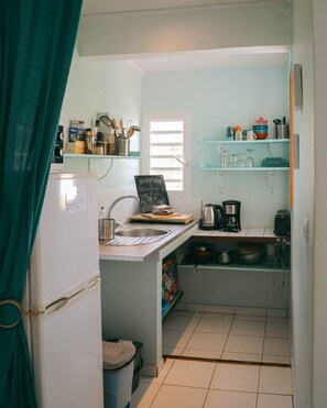 Una cocina compacta con refrigerador, pileta y diversos electrodomésticos.