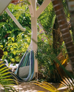A hammock hanging from a white structure surrounded by lush green foliage.
