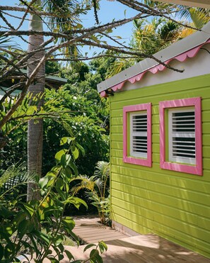 A small, single-story building with a green exterior and pink window frames, surrounded by lush tropical vegetation.