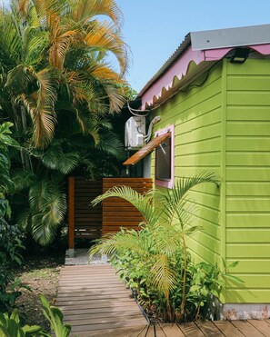 Un bâtiment écologique doté d’une terrasse en bois menant à une porte, le tout entouré d’une végétation tropicale luxuriante.