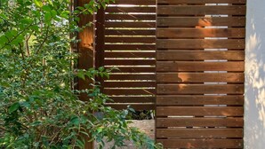 Une porte en bois avec des lattes horizontales, un chemin pavé et un mur à l’extérieur blanc.