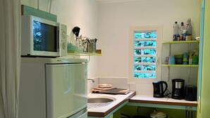 Une cuisine compacte équipée d’un réfrigérateur, d’un four à micro-ondes et d’un évier. On y trouve des étagères avec des ustensiles de cuisine et une fenêtre avec des stores.