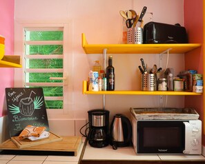 Una cocina con cafetera, microondas y un cartel en la pizarra.
