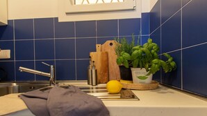 Een keuken met blauwe tegels, een spoelbak, een snijplank, een citroen, een mes, een houten snijplank en een pot met basilicum.