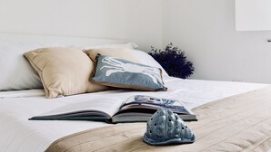 Een net opgemaakt bed met een beige en witte kussensloop, een blauw-witte kussensloop, en een paar schoenen op het bed.