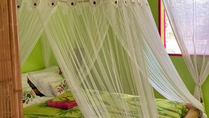 Ein Zimmer mit einem Bett unter einem weißen Baldachin, grünen Wänden und einem Fenster mit Vorhang.