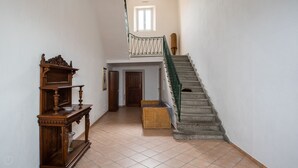 Un couloir avec une console en bois, un banc en osier et un escalier en pierre.