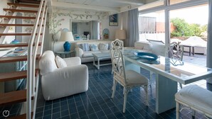 Uma sala de estar ampla com sofá, mesa de jantar com cadeiras, escada e vista para o exterior.