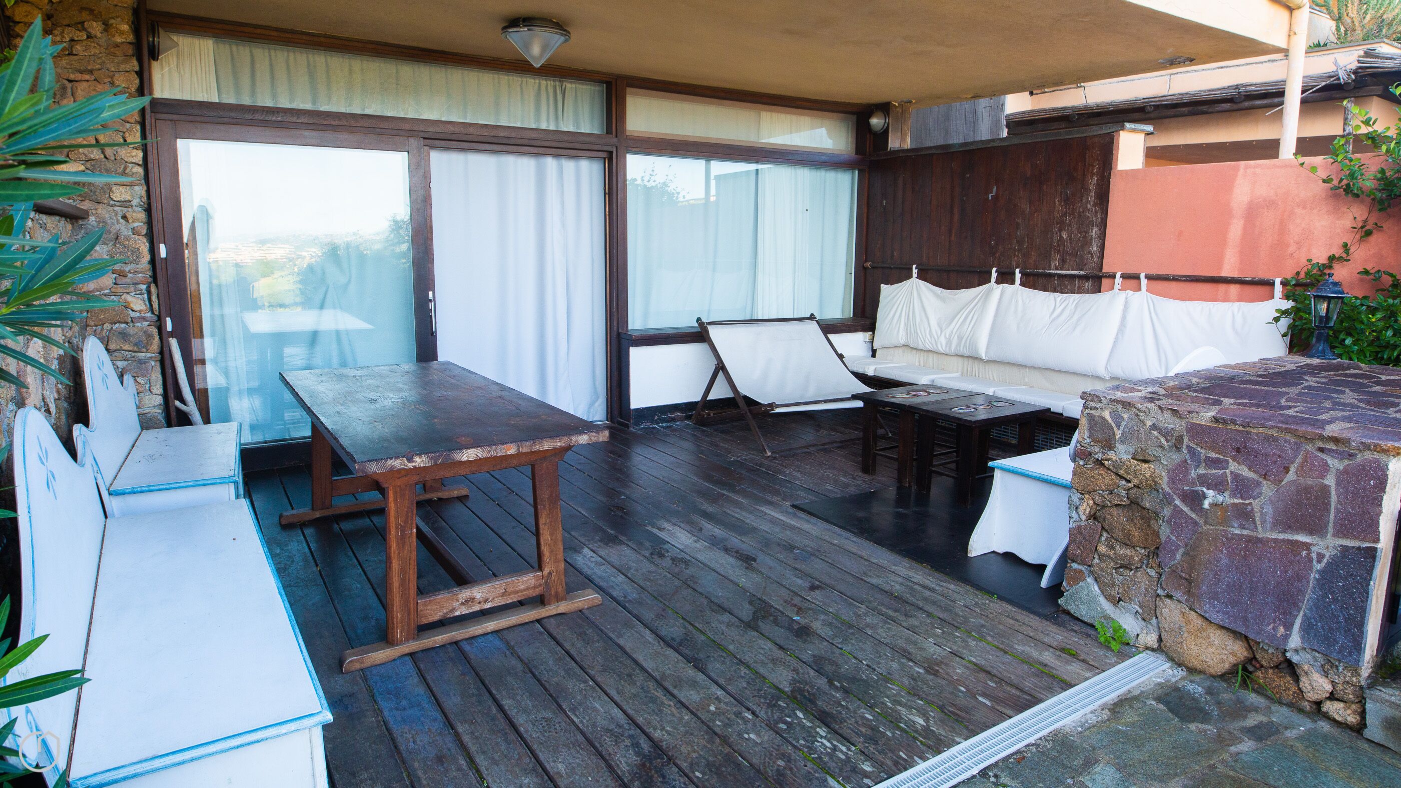 Eine Terrasse im Freien mit Holztisch, gepolsterten Sitzgelegenheiten und einem Steinkamin.