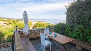 Um pátio externo com mesa e cadeiras, um muro de pedra e vista para o mar.
