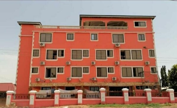 A multi-story building with a red facade, multiple windows, and air conditioning units.