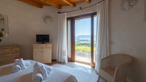A bedroom with a bed, a television on a wooden cabinet, and a view of the sea through a glass door. - Villa Acqua Marina - Four Bedroom Villa, Sleeps 8 (Golfo Aranci)
