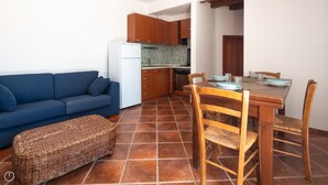 A compact living space with a sofa, a dining table with chairs, a kitchen area, and a tiled floor. - Mediterranea - One Bedroom Apartment, Sleeps 4 (Loiri)