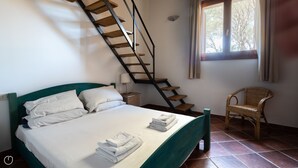 A bedroom with a bed, a chair, a nightstand, a lamp, a window, and a wooden staircase. - Mediterranea - One Bedroom Apartment, Sleeps 4 (Loiri)