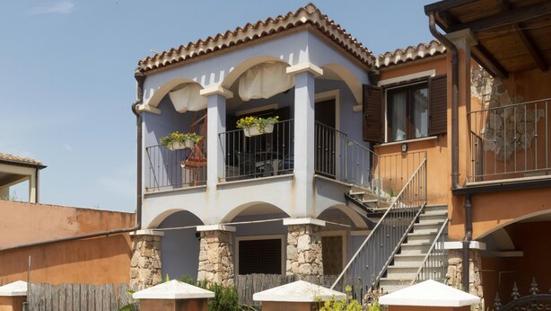 A two-story building with a balcony, stone pillars, and a staircase leading to the upper floor. - Nido Blu Tortolì | Terrace, Hammock & Park (Tortoli)