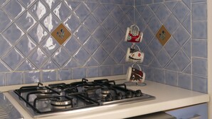 A kitchen with a gas stove, blue patterned tiles, and decorative mugs on a rack. - Nido Blu Tortolì | Terrace, Hammock & Park (Tortoli)