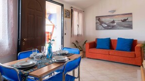 A dining area with a table set for four, a sofa, and a painting of a boat on the wall. - Nido Blu Tortolì | Terrace, Hammock & Park (Tortoli)