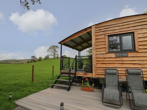 A wooden cabin with a deck, a sign reading "WILD ACRE", and a view of a green field. - Wild Acre (Llangadog)