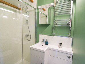 A bathroom with a glass shower enclosure, a white sink with a mirror above it, and a towel rack. - Wild Acre (Llangadog)