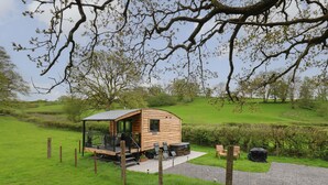 A wooden cabin with a covered porch, outdoor seating, and a gravel path leading to it. - Wild Acre (Llangadog)