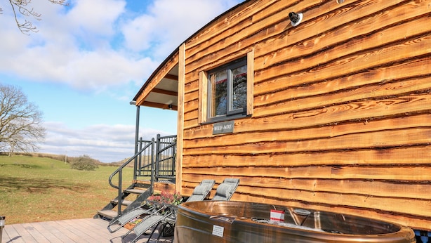 A wooden cabin with a hot tub and outdoor seating. - Wild Acre (Llangadog)