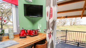 A kitchen with a wooden countertop, a red kettle, a toaster, and a television mounted on the wall. - Wild Acre (Llangadog)