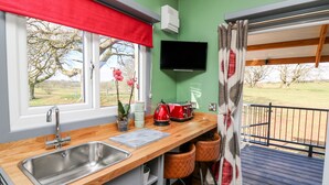 A kitchen with a wooden countertop, stainless steel sink, and a window with a red valance. There is a potted plant, a kettle, and a television on the wall. - Wild Acre (Llangadog)