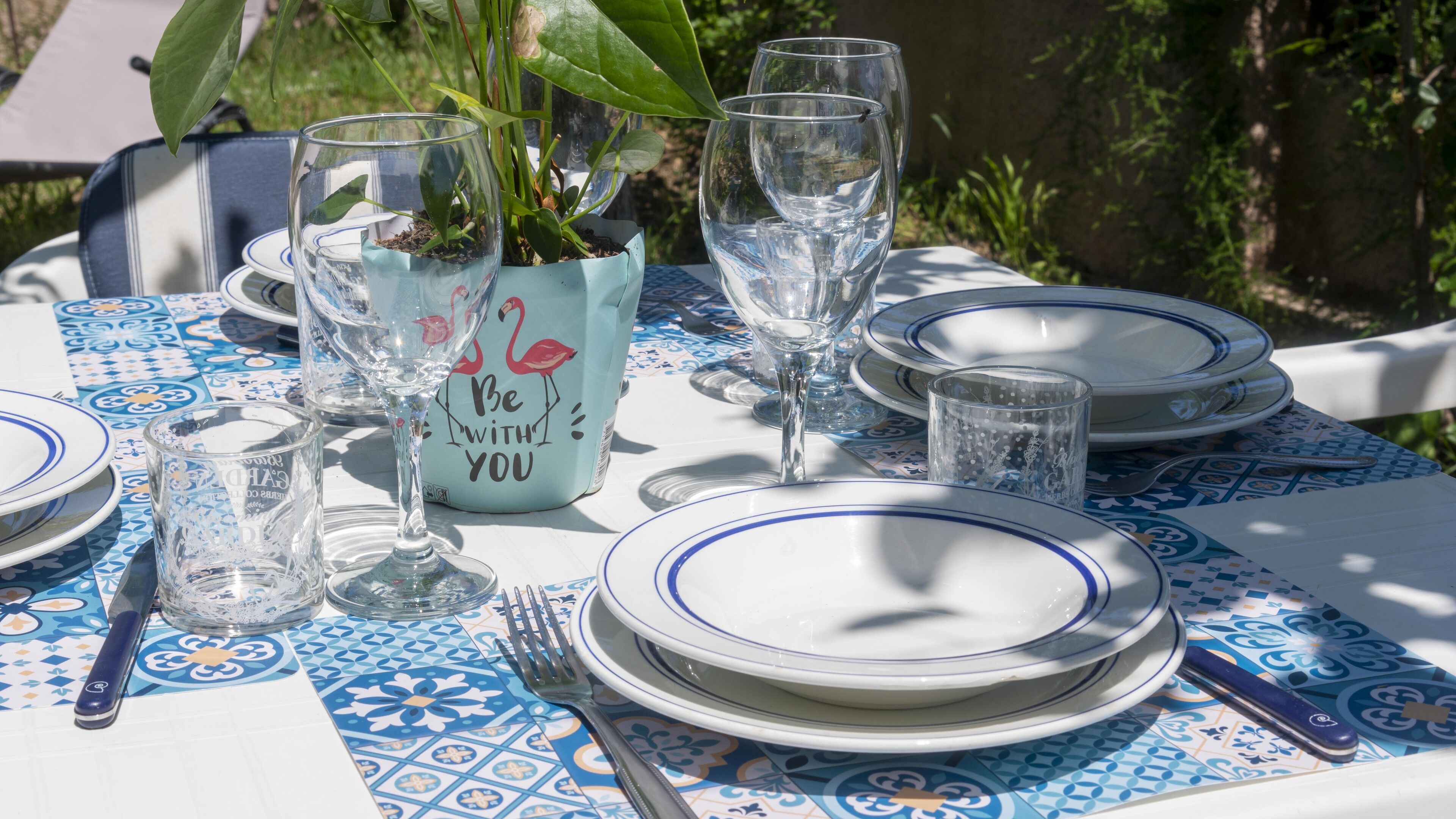 Een gedekte tafel met borden, glazen en bestek, met een blauw-wit geruit tafelkleed.