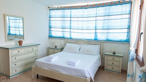 Un dormitorio con una cama, dos mesitas de noche, un aparador, un espejo y una ventana con cortinas azules.