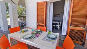 An outdoor dining area with a table set for two, surrounded by orange chairs, and wooden shutters on the sides. - La Casa Di Rita - B - Lu Nibbaru (Muriscuvò)