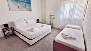 A hotel room with a double bed, a single bed, a small table with a lamp, a chair, and a painting of a beach scene. - La Casa Di Rita - B - Lu Nibbaru (Muriscuvò)
